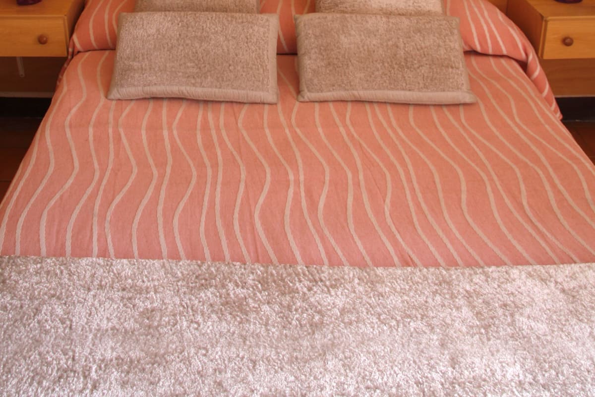 A neatly made bed with striped bedding, two bedside tables with lamps, and framed pictures on the wall.