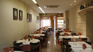 Un restaurante con varias mesas dispuestas para comer, con servilletas anaranjadas y manteles blancos.