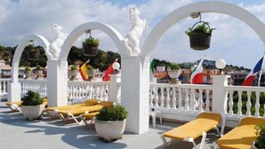 A rooftop terrace with white arches, potted plants, and yellow sun loungers. Flags are visible in the background. - Las Americas (Blanes)