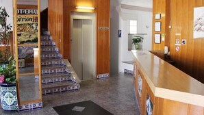 A hotel lobby with a wooden reception desk, a staircase with patterned steps, and a tiled floor. - Las Americas (Blanes)
