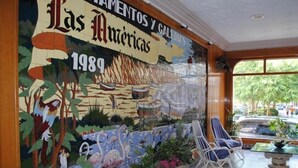 A mural with a tropical theme, a seating area with chairs, and a view of the street outside. - Las Americas (Blanes)