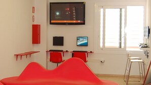 Una habitación moderna con una televisión de pantalla plana, asientos rojos y una ventana con persianas.