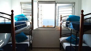 Una habitación con literas, una ventana con persianas y vista al mar.