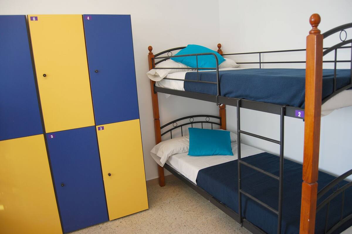 Een stapelbed met twee niveaus, elk met een blauwe matras en een kussen. Aan de rechterkant bevindt zich een houten trap.