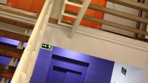 Una escalera con barandillas blancas y paredes anaranjadas que conduce a una puerta con un letrero de salida verde.