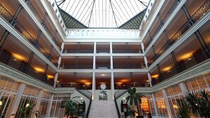 Een statig atrium met een centrale trap, meerdere balkons en een grote glazen koepel.