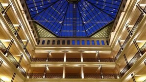 Een statig atrium met een glazen koepel, meerdere verdiepingen en een centrale trap.
