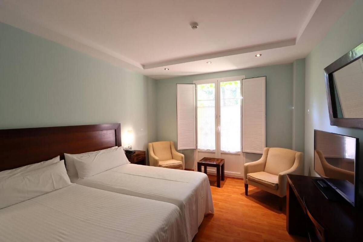 A hotel room with two beds, a TV, a desk, and two chairs.