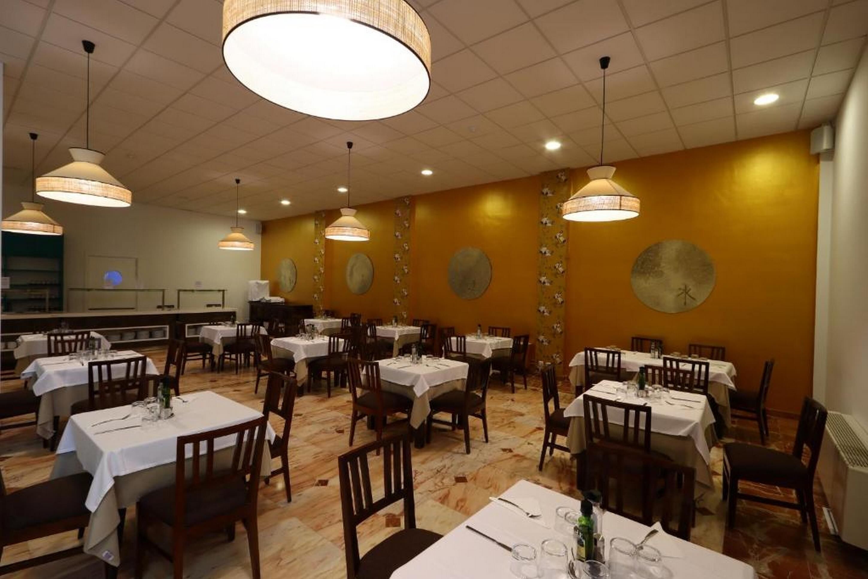 Un comedor con varias mesas y sillas, lámparas colgantes grandes y decoración en las paredes.