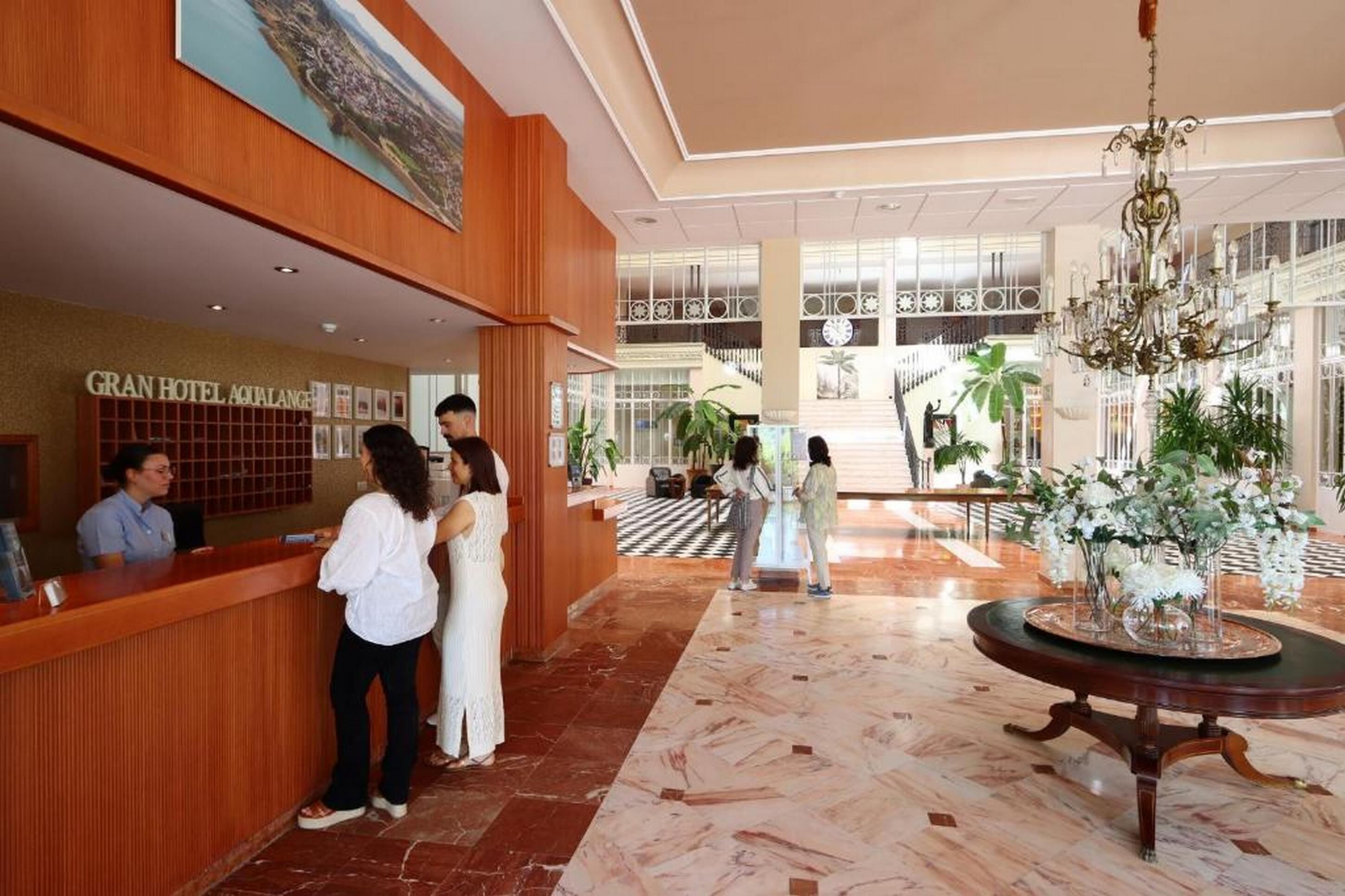 Un vestíbulo de hotel con una recepción, una escalera imponente y un candelabro.