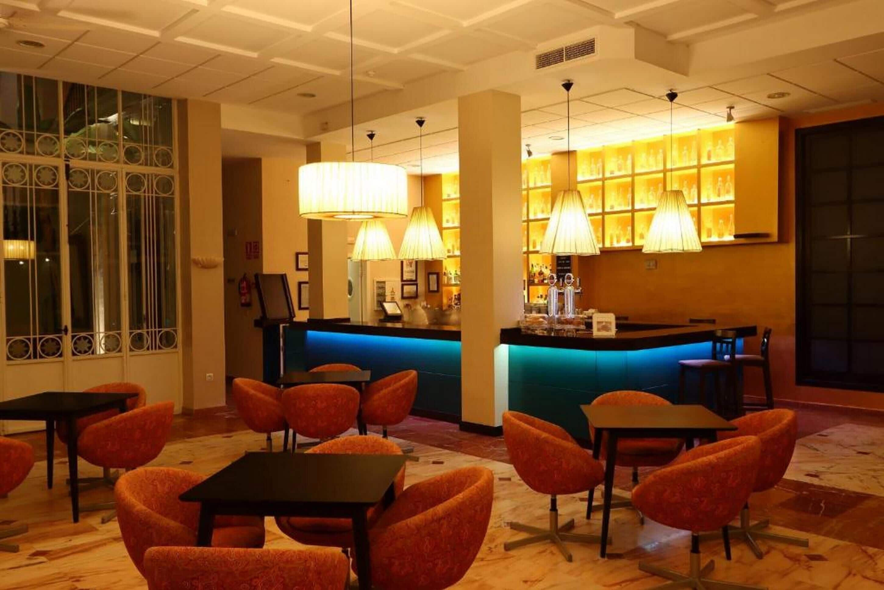 A lobby with a reception desk, orange chairs, and a bar area with illuminated shelves.