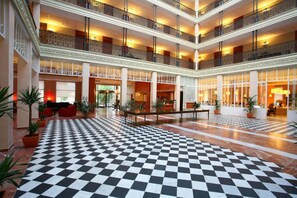 Eine geräumige Lobby mit Schachbrettmuster-Boden, mehreren Balkonen und einer zentralen Sitzecke.