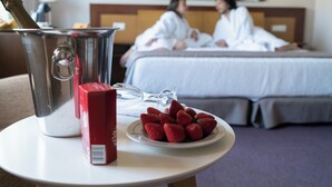 A hotel room with a bed, a bedside table with a champagne bottle, a red box, and a plate of strawberries. - El Salugral Termal Resort (Hervas)