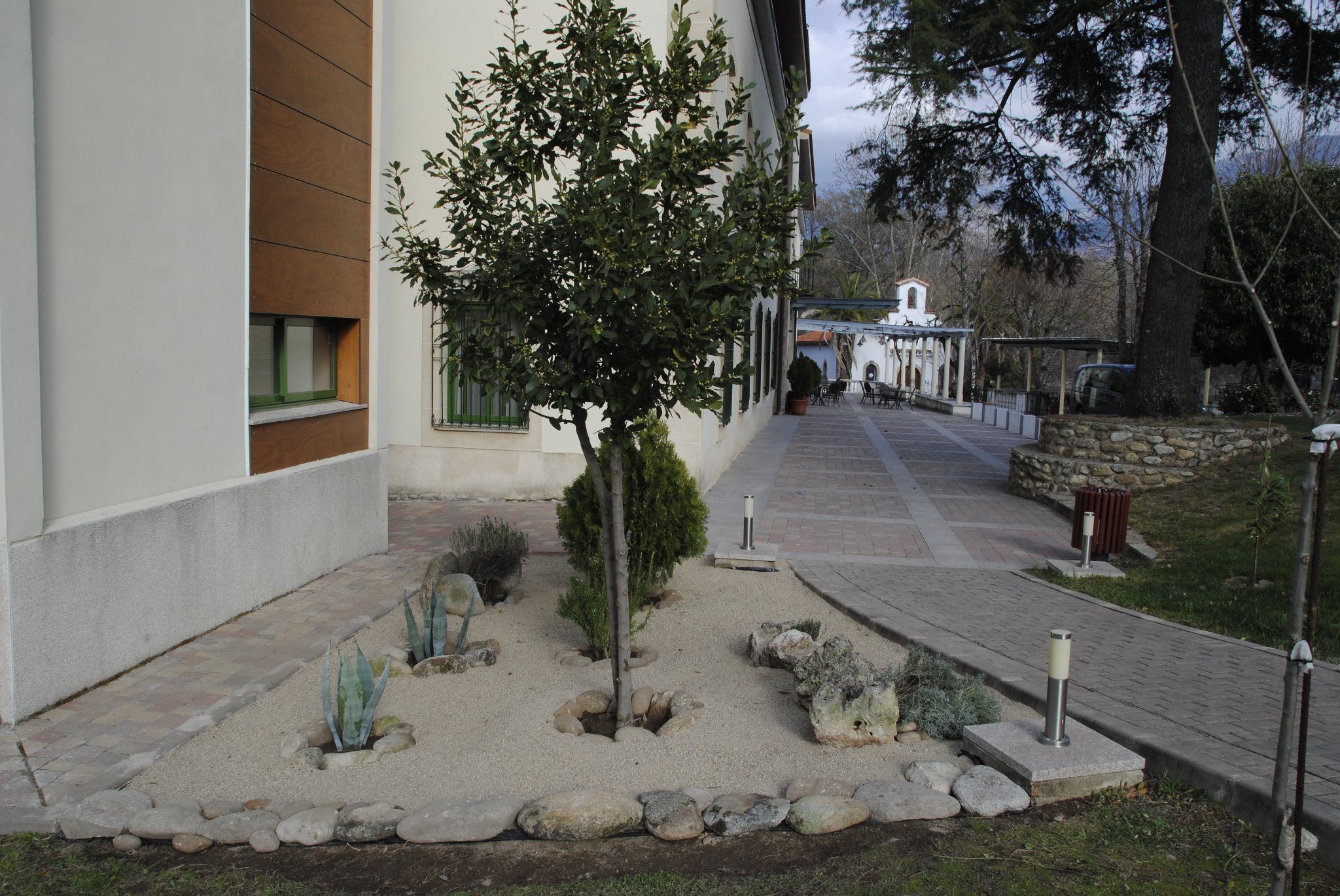 Un jardín ajardinado con un sendero que lleva a un edificio de fachada blanca y paneles de madera.