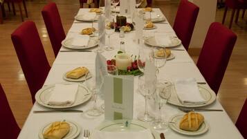 Una mesa de comedor lista para una comida, con manteles blancos, sillas tapizadas en rojo y platos, vasos y cubiertos ordenados.