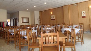 Un amplio comedor con mesas y sillas de madera, un techo alto con luces enrejadas y paneles de madera en las paredes.