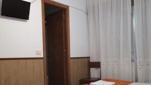 Habitación de hotel con dos camas, cabecera de madera, televisor de pantalla plana en la pared y ventana con cortinas blancas.