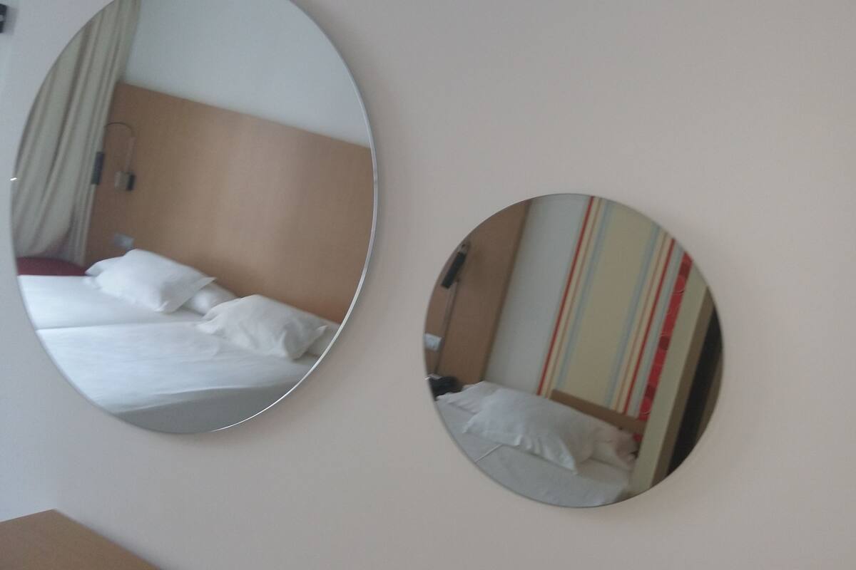 Two circular mirrors on a wall, reflecting a bed with white bedding and a striped wall behind it.