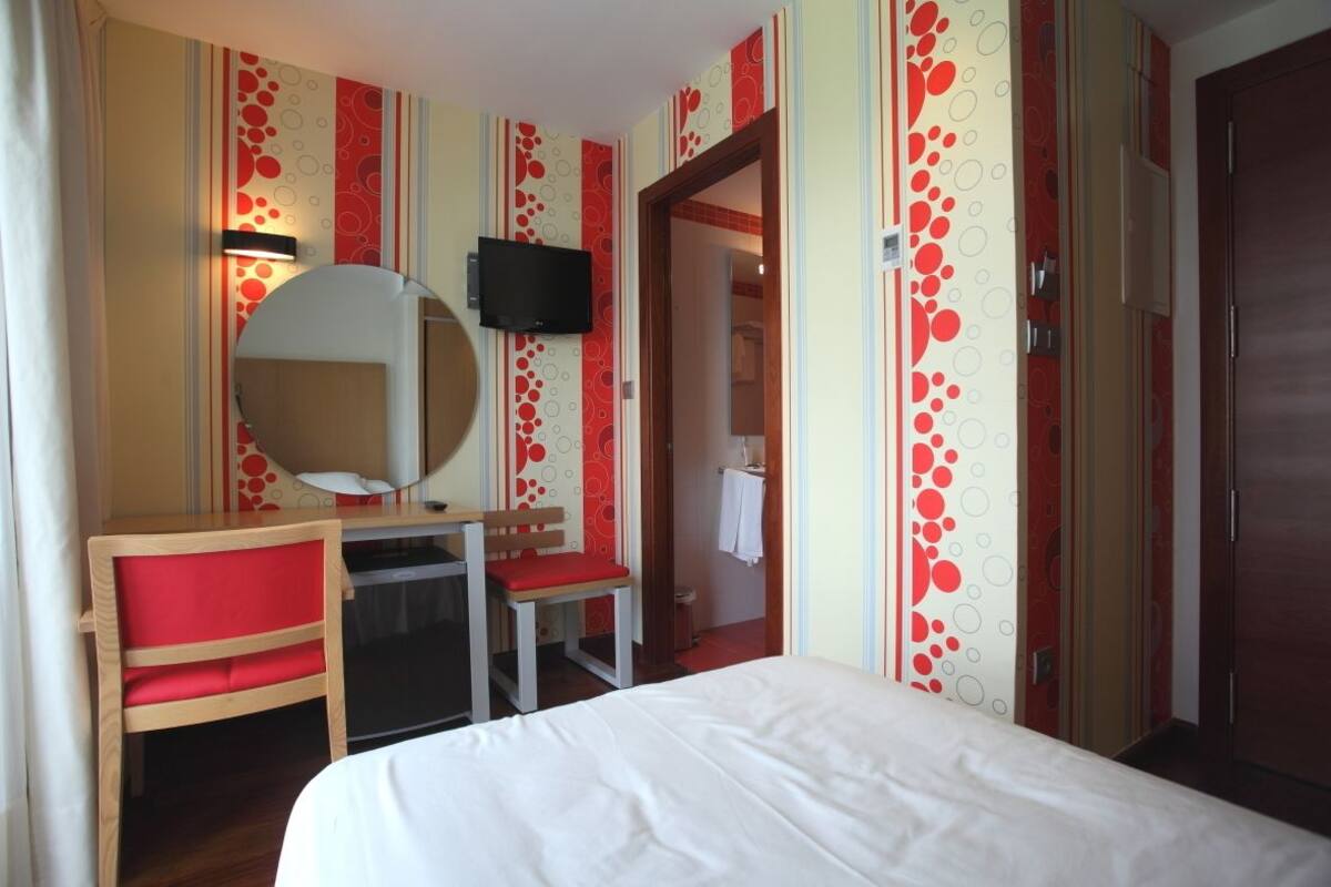 A hotel room with a bed, a desk with a chair, a television, and a mirror.