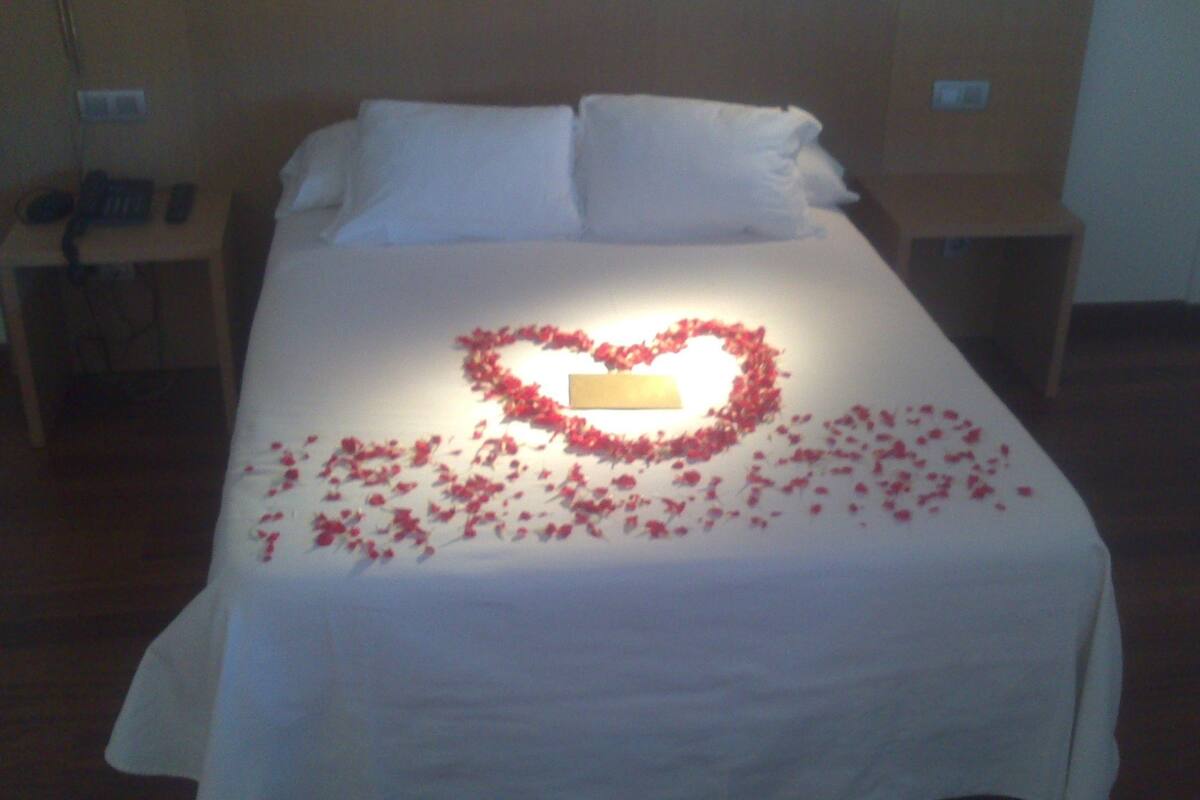 A bed with a heart-shaped arrangement of rose petals and a card in the center.