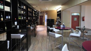 Zona de bar con estanterías llenas de botellas, taburetes blancos y una mesa roja con sillas.