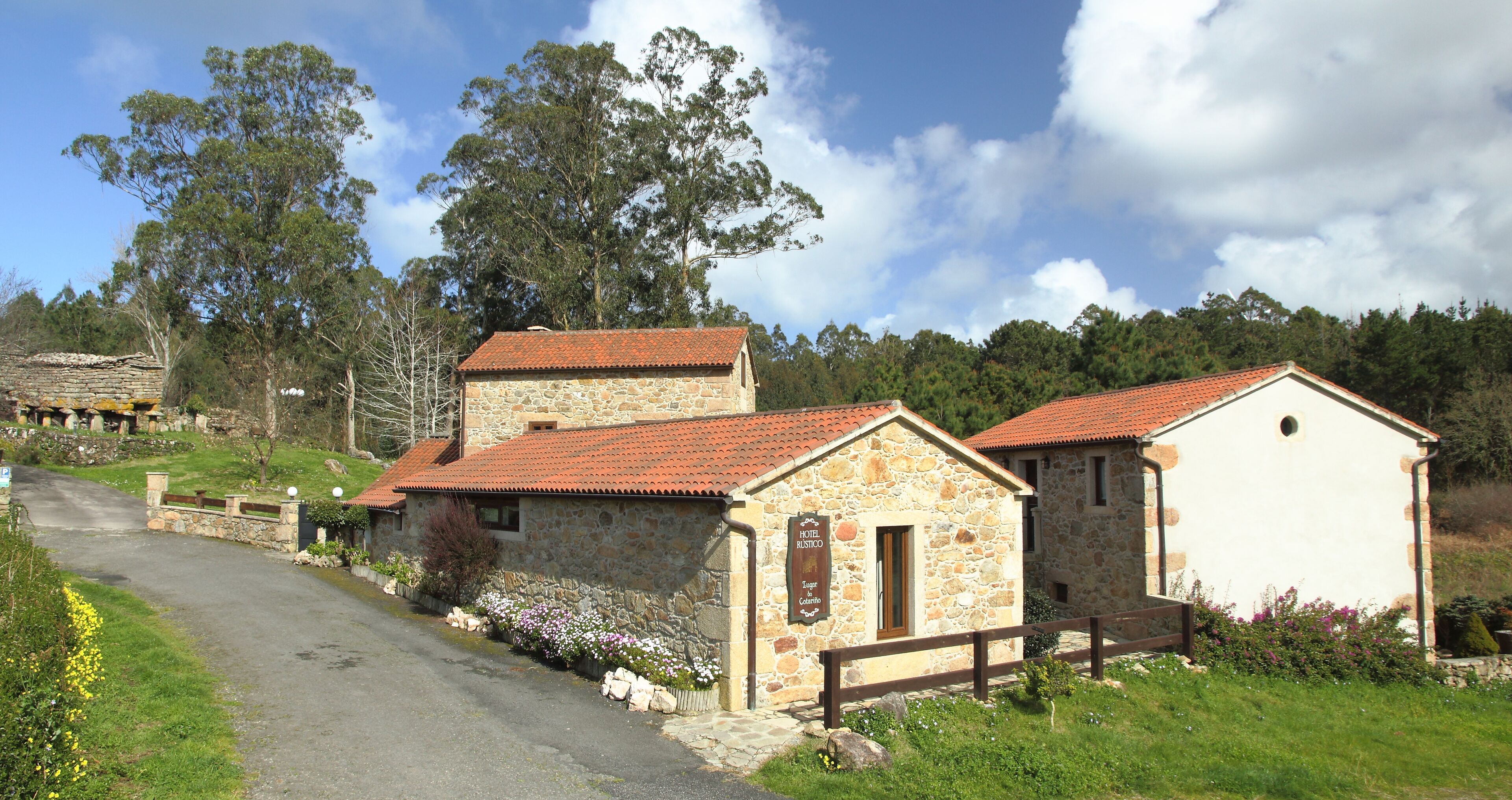 A stone building with a red-tiled roof, a sign indicating it is a hotel, and a wooden fence in front.