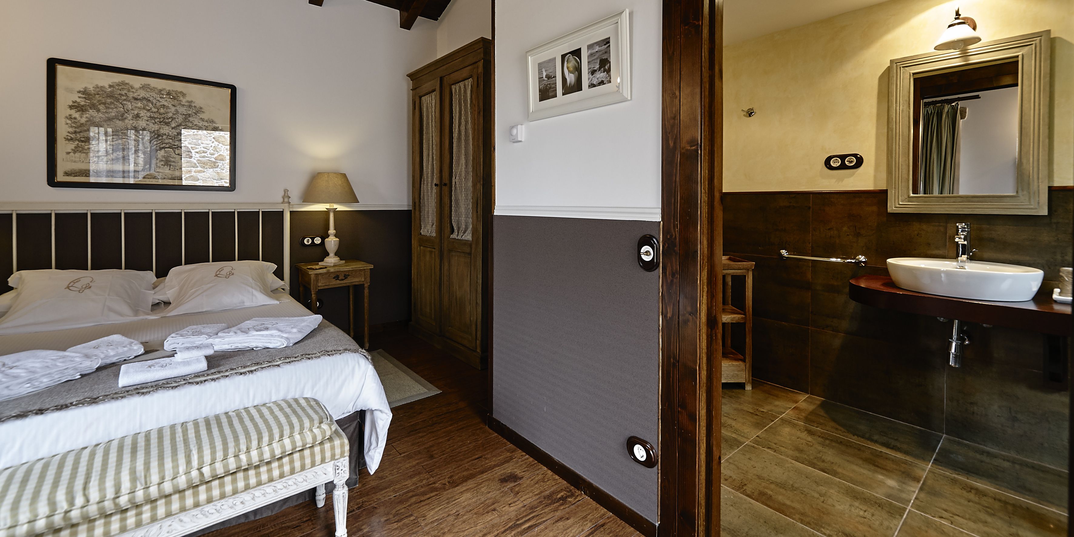 Ein Schlafzimmer mit Bett, Nachttisch, Lampe sowie ein Badezimmer mit Waschbecken und Spiegel.