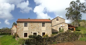 A stone house with a red-tiled roof, multiple windows, and a stone wall in front.