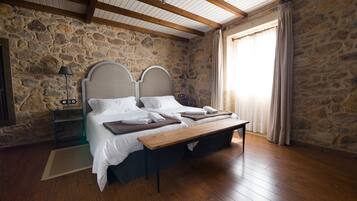 A bedroom with a stone wall, wooden beams, a bed with white linens, a bedside table, and a nightstand.