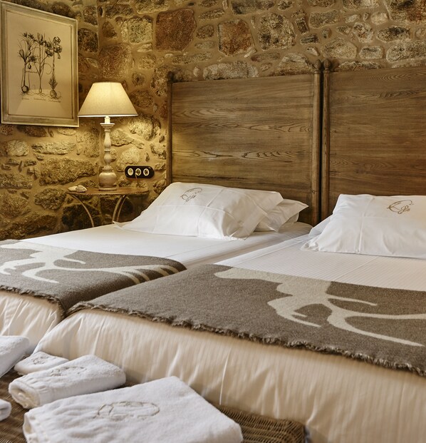 A double bed with a wooden headboard, a bedside table with a lamp, and a stone wall.