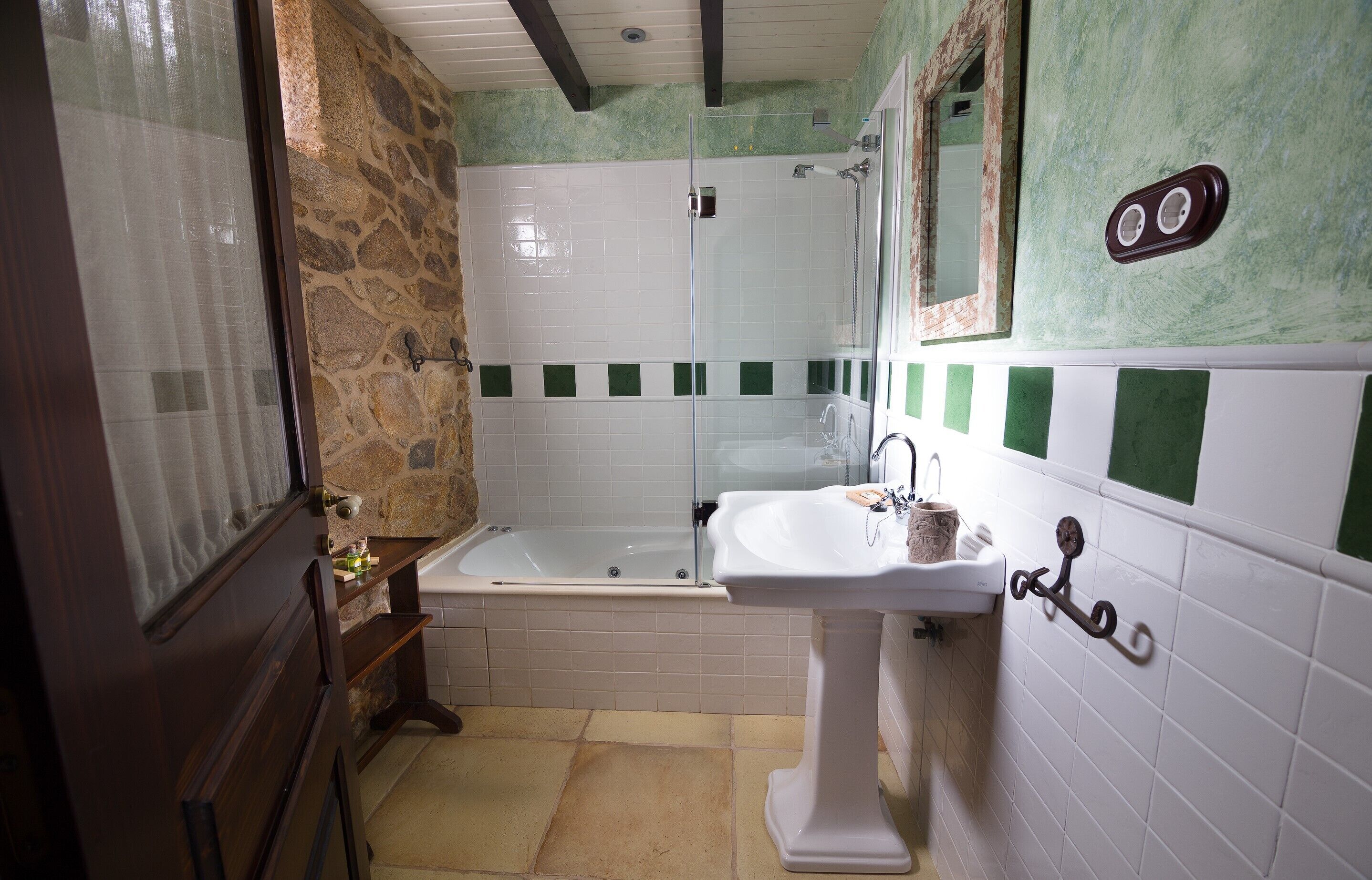 A bathroom with a stone wall, a bathtub, a sink, and a mirror.