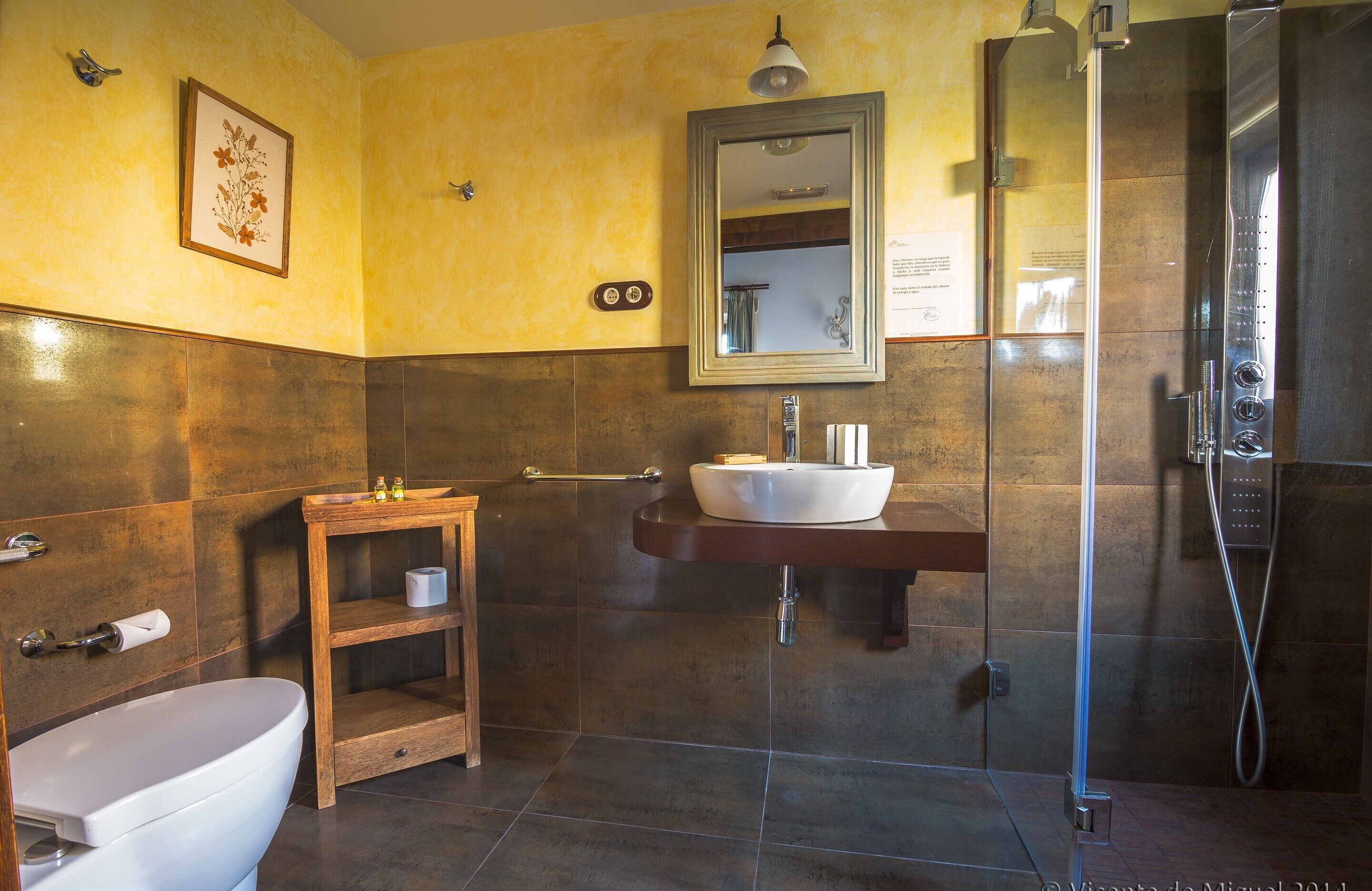 Een badkamer met een wit toilet, een houten wastafelmeubel met een wastafel en een douchecabine met glazen wanden.
