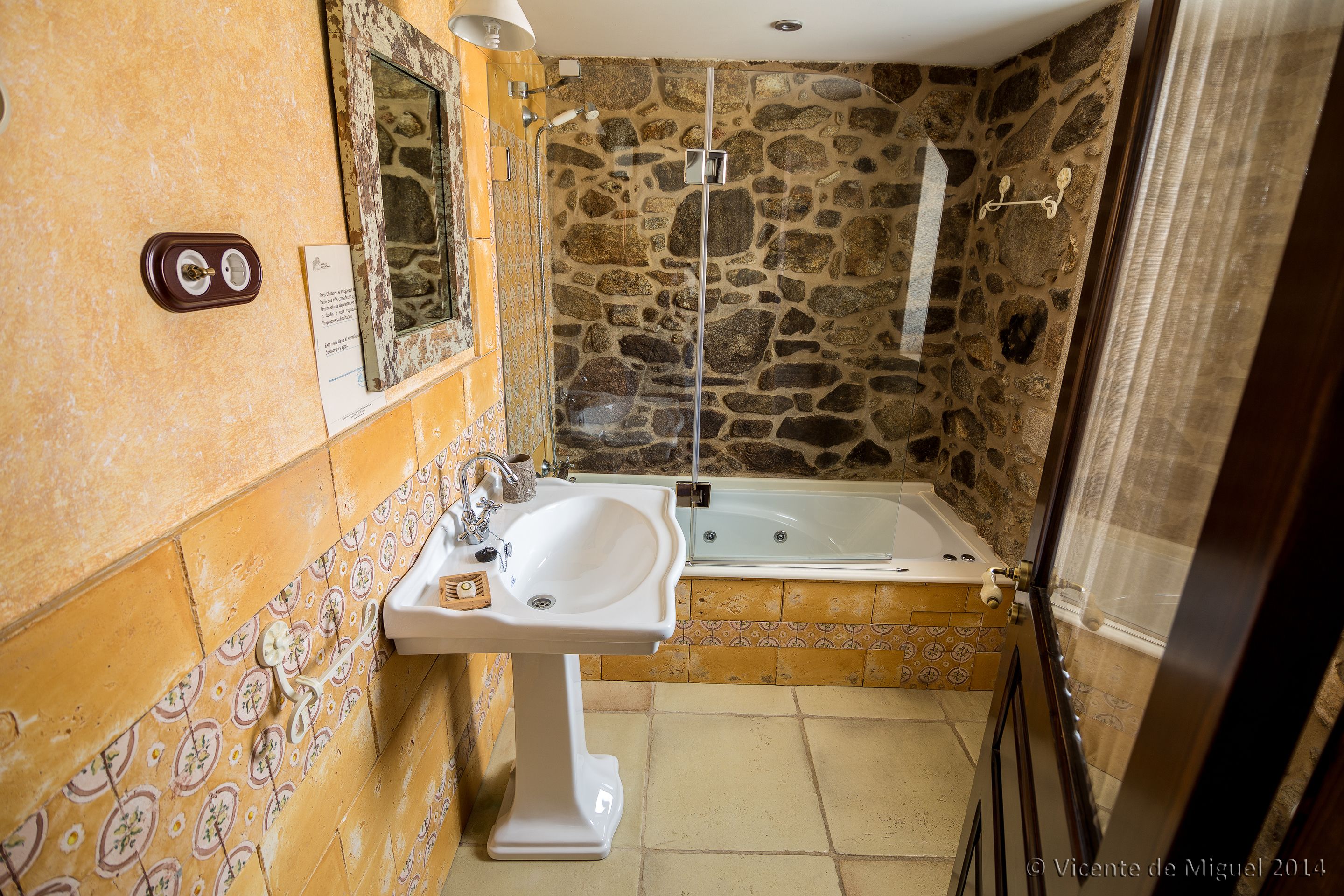 A bathroom with a stone wall, a bathtub, and a sink with a mirror.