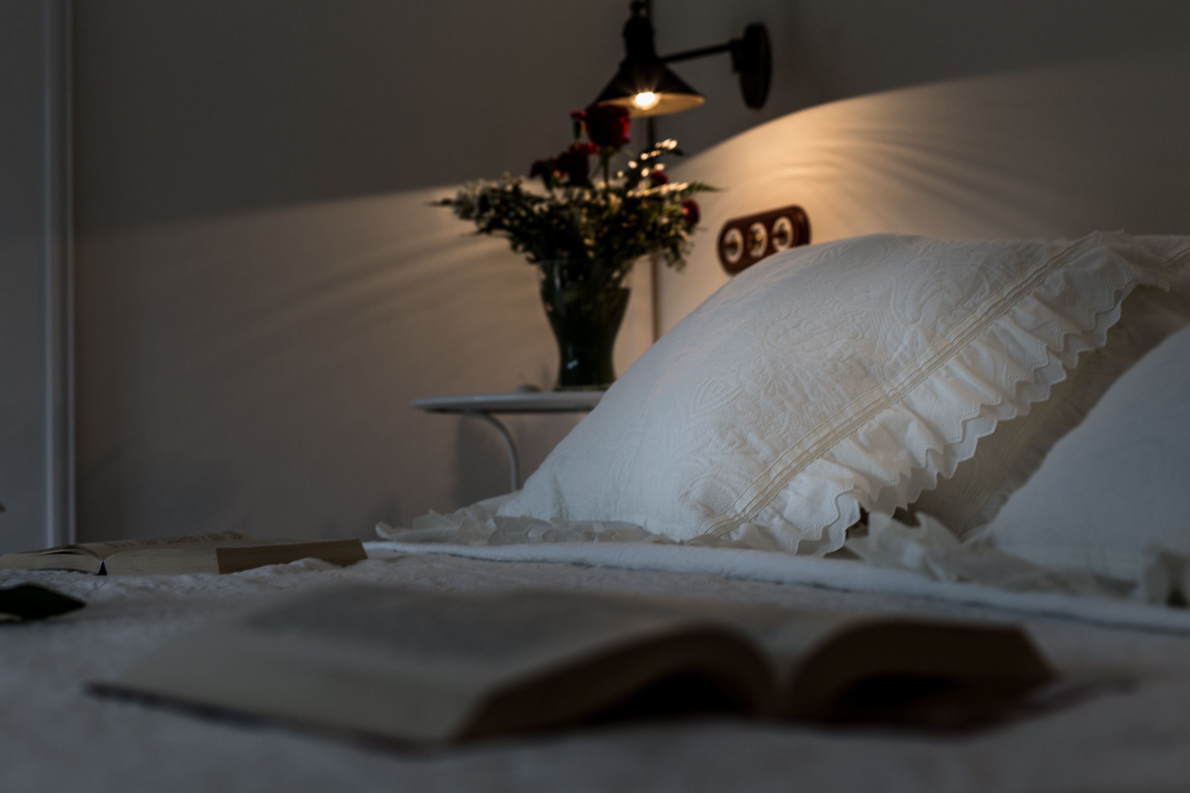 A bedroom with a bed, an open book, a bedside lamp, and a wall clock.