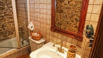 Un baño con pared de piedra, espejo con marco de madera, lavamanos, inodoro y bañera.