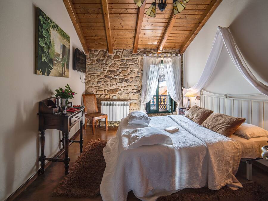 Quarto com parede de pedra, cama com roupa de cama branca, teto de madeira e um quadro na parede.