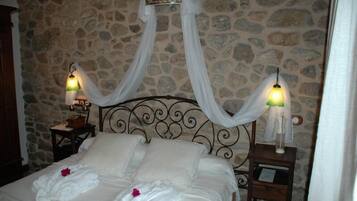 Una cama con ropa blanca y dosel, dos lámparas de noche y un fondo de pared de piedra.
