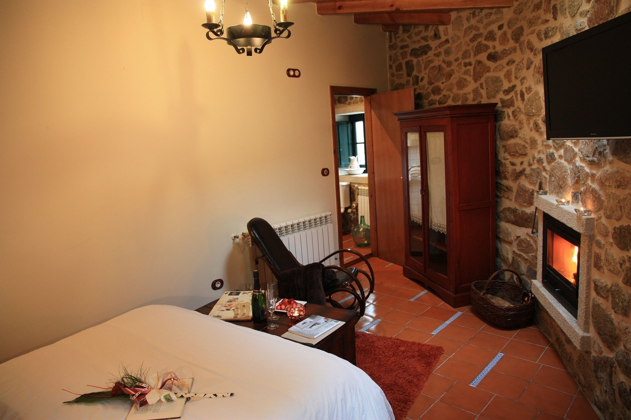 A bedroom with a bed, a chair, a fireplace, and a stone wall.