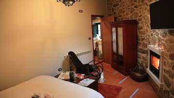 A bedroom with a bed, a chair, a fireplace, and a stone wall.