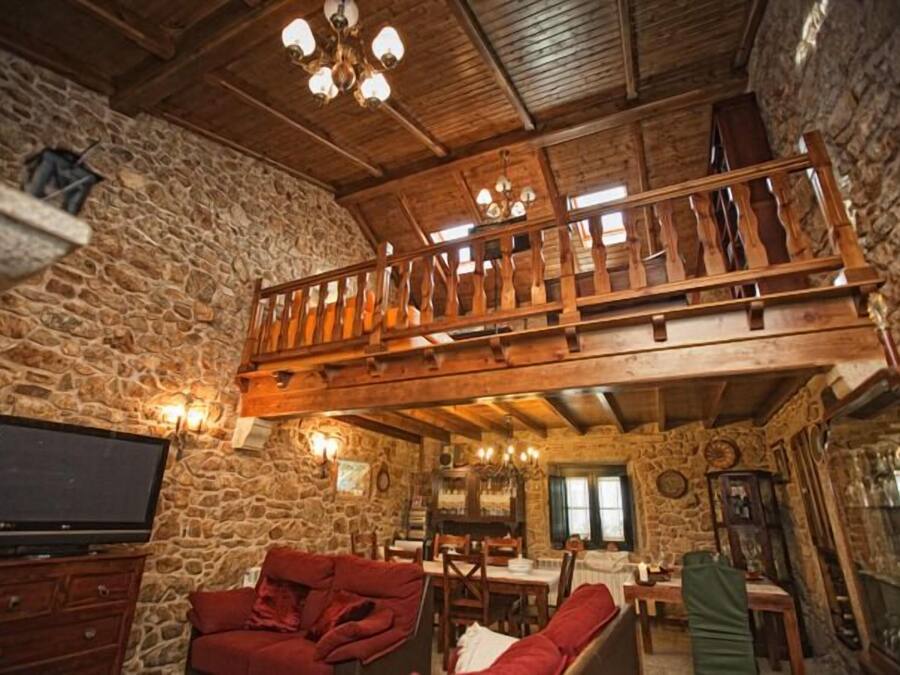 Un interior rústico con paredes de piedra, un balcón de madera, un televisor y un comedor.