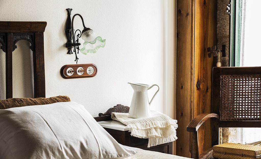 A cozy room with a wooden bed, a white pitcher on a small table, and a vintage wall lamp.