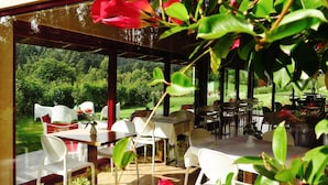 Eine Terrasse im Freien mit Tischen und Stühlen, umgeben von Grünpflanzen und Blick auf einen üppigen Garten.