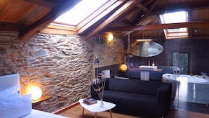 Ein modernes Schlafzimmer im Loft-Stil mit Steinwand, schwarzem Sofa, weißem Bett und einem Oberlicht.