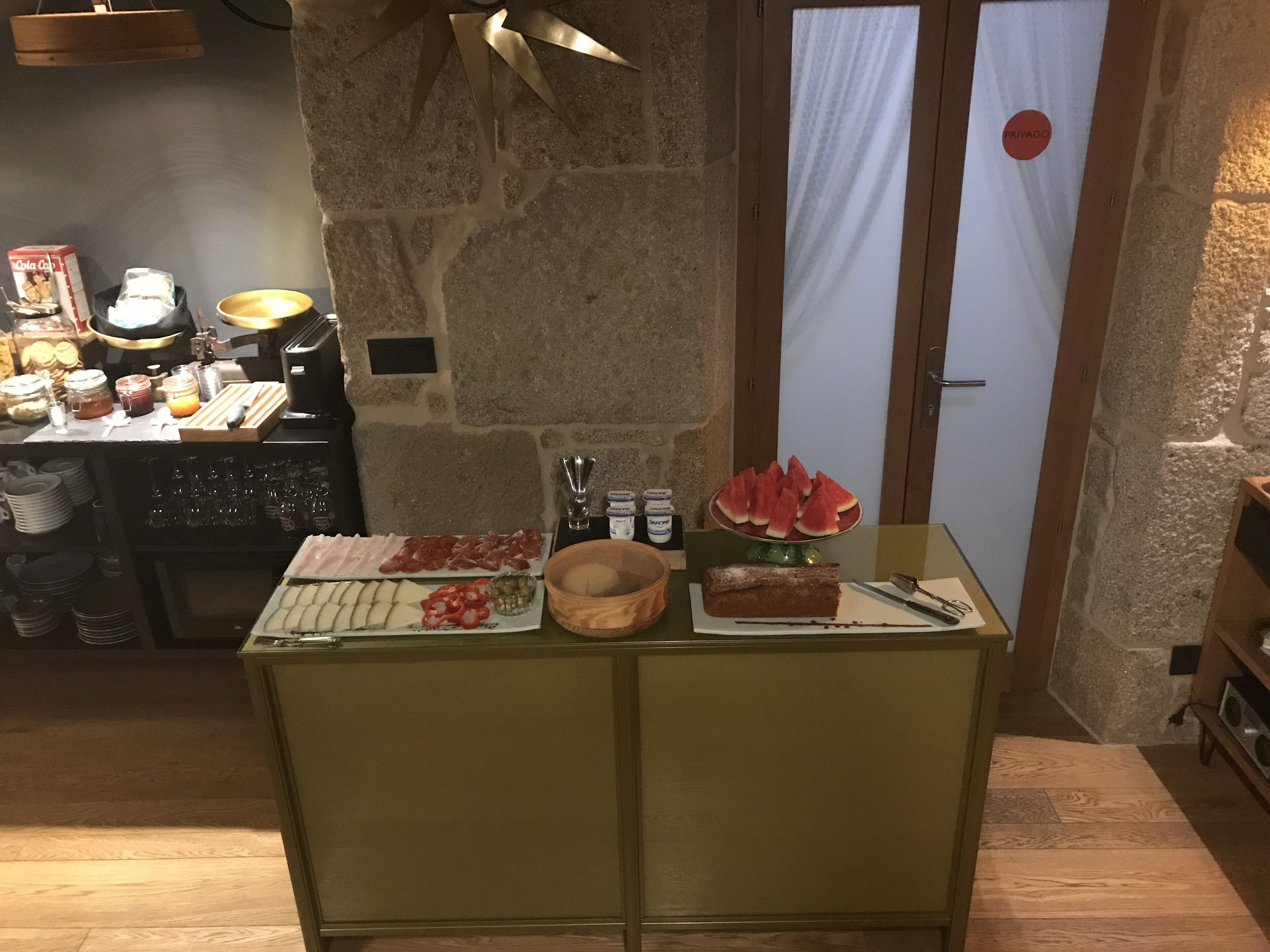 A breakfast buffet with various food items and a dessert on a table in a stone-walled room.