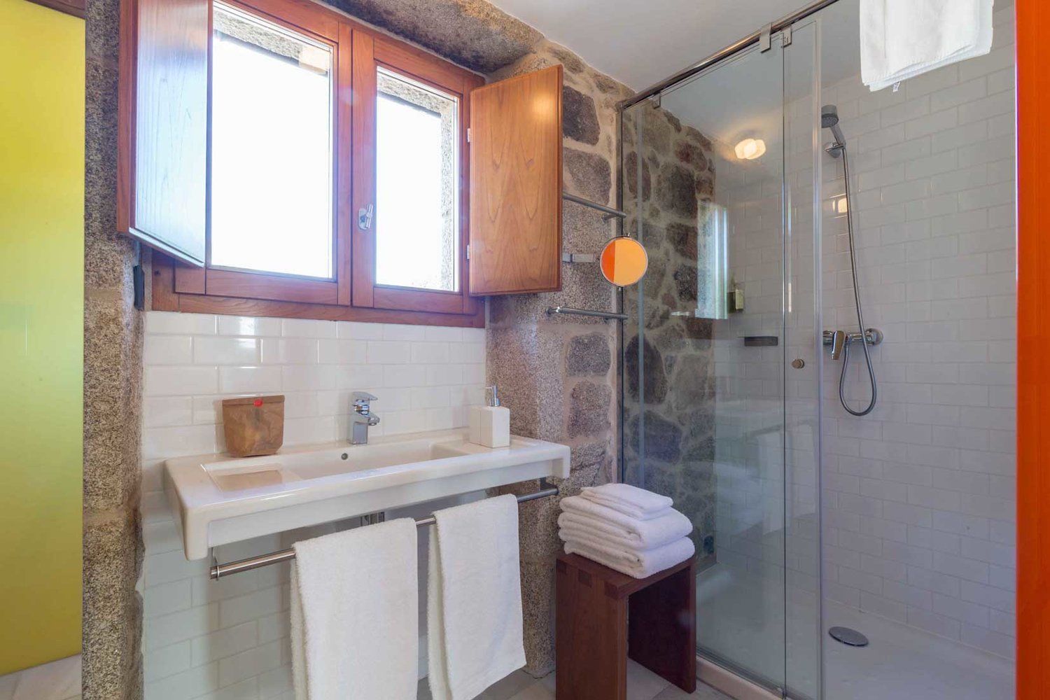 A bathroom with a stone wall, a wooden cabinet, a sink, and a glass shower enclosure.