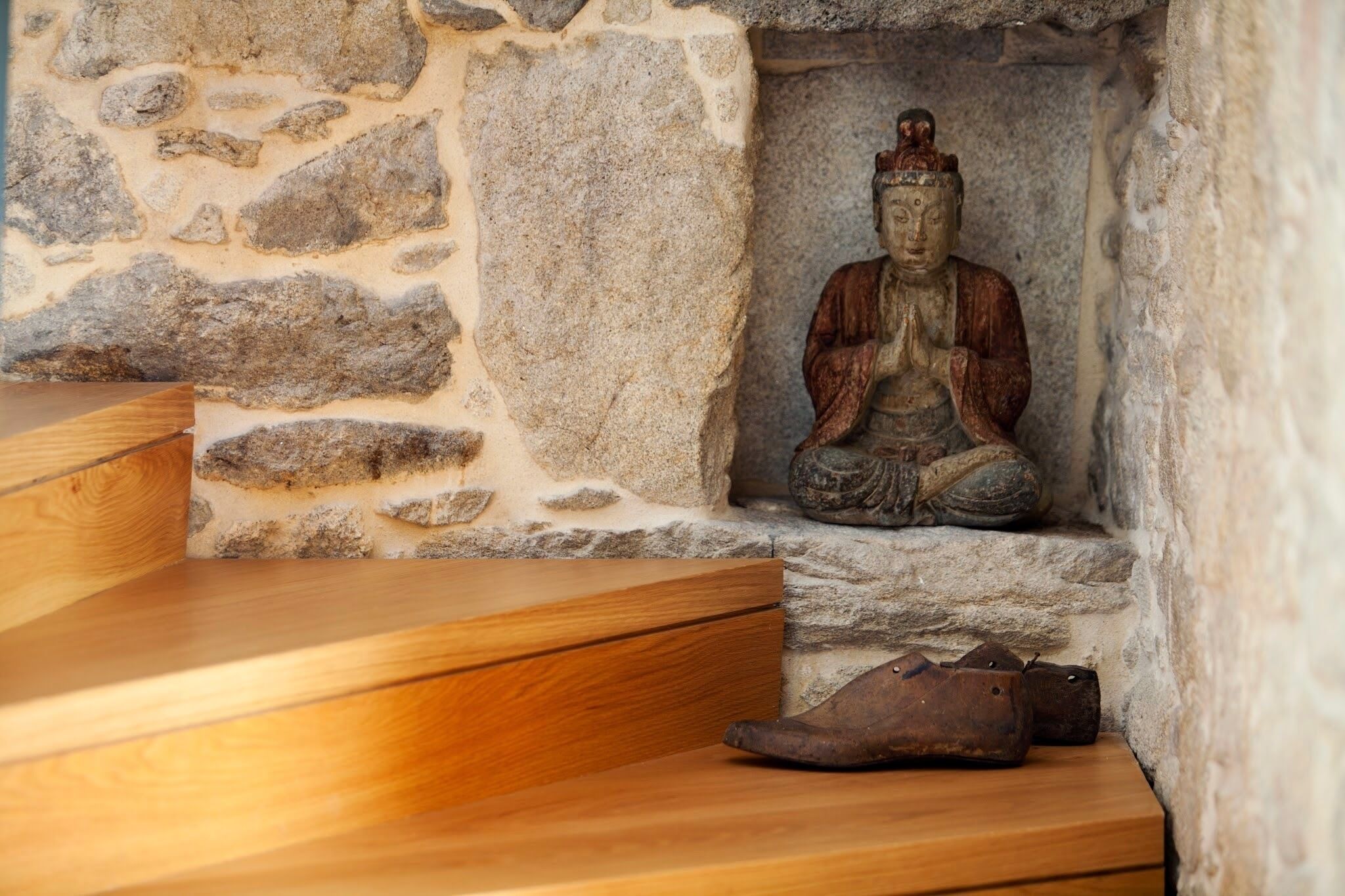 A stone wall with a statue of a seated figure, wooden steps, and a pair of shoes on the ground.