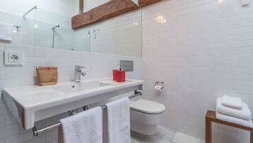 A modern bathroom with a large mirror, two sinks, a toilet, and a wooden shelf above the mirror.