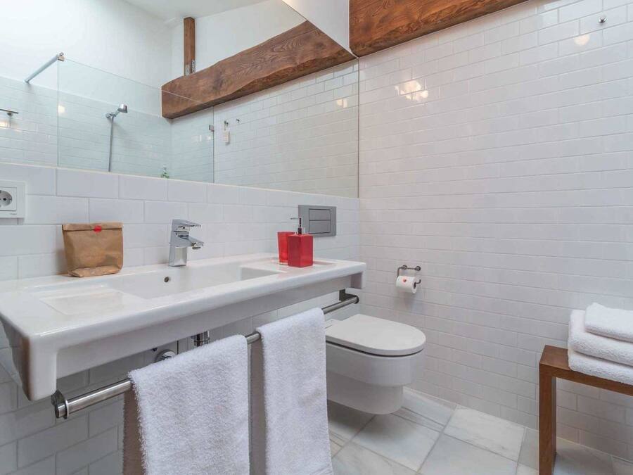 A modern bathroom with a large mirror, two sinks, a toilet, and a wooden shelf above the mirror.
