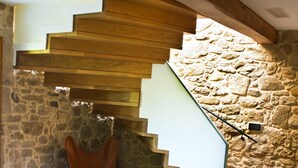 A modern interior with a wooden staircase, stone walls, and a leather sofa. - Os Lambráns (Padron)
