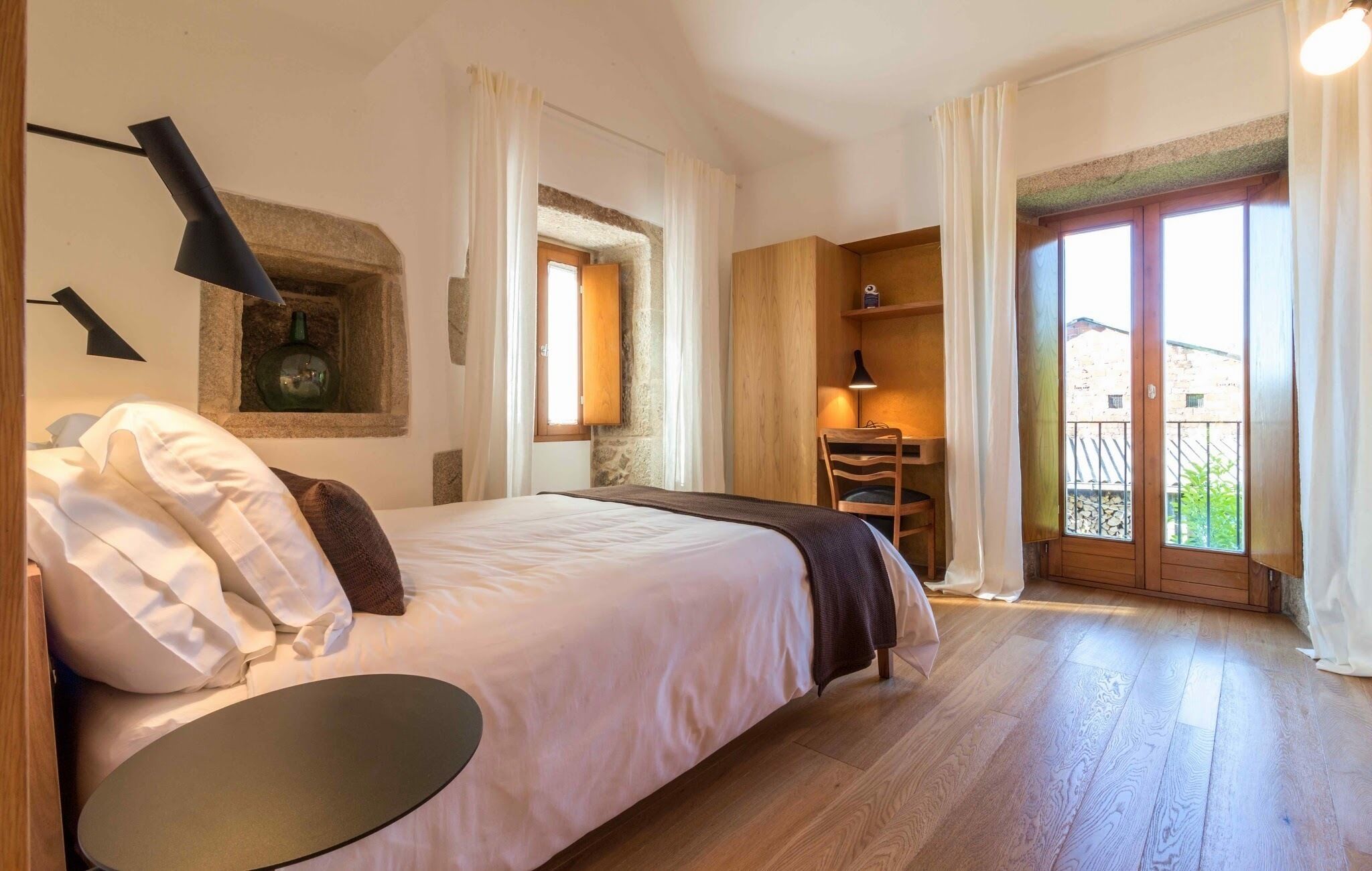 Een slaapkamer met een bed, een bureau en een balkon.